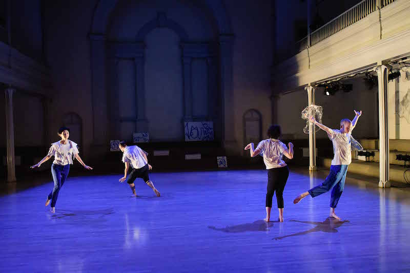 Four dancers in cat t-shirts run around the sanctuary of St. Mark's Church under royal blue lights